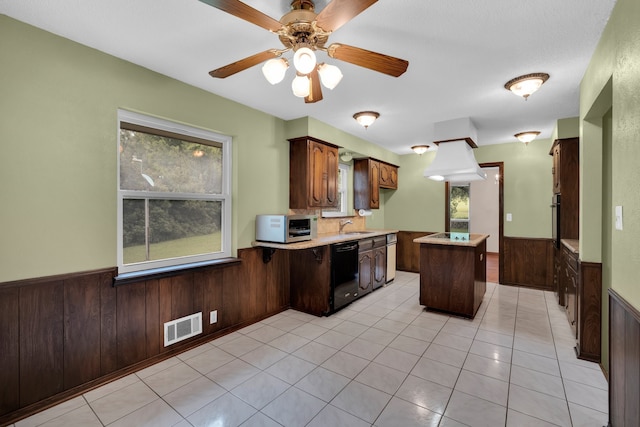 kitchen featuring dishwasher, wood walls, a center island, ceiling fan, and light tile patterned floors