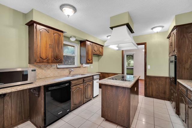 kitchen featuring island exhaust hood, a wainscoted wall, a kitchen island, black appliances, and a sink