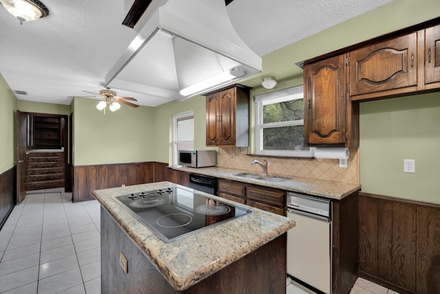 kitchen featuring black appliances, a kitchen island, a wainscoted wall, a sink, and wooden walls