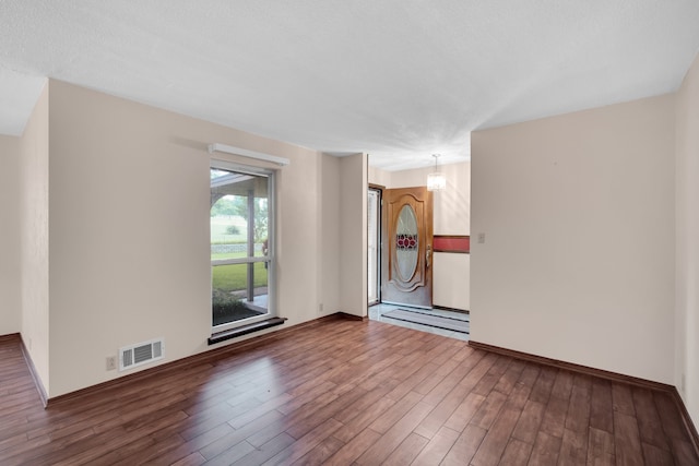 unfurnished room featuring a textured ceiling, dark hardwood / wood-style flooring, and an inviting chandelier