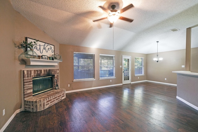 unfurnished living room with ceiling fan with notable chandelier, a brick fireplace, vaulted ceiling, dark hardwood / wood-style floors, and a textured ceiling