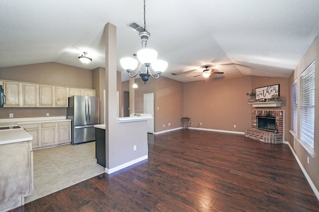 kitchen featuring ceiling fan with notable chandelier, vaulted ceiling, light hardwood / wood-style flooring, a fireplace, and stainless steel refrigerator