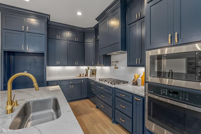 kitchen with custom exhaust hood, stainless steel appliances, sink, light stone counters, and light hardwood / wood-style flooring