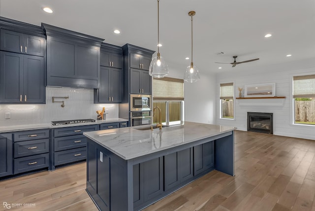 kitchen with a large island, appliances with stainless steel finishes, a fireplace, hanging light fixtures, and sink