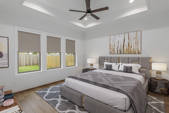 bedroom featuring a raised ceiling, ceiling fan, and light hardwood / wood-style flooring