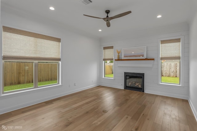 unfurnished living room with ceiling fan, a large fireplace, and light wood-type flooring