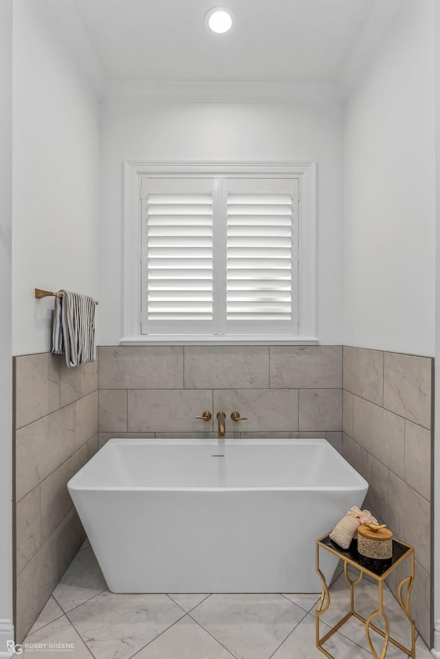 bathroom with tile walls, ornamental molding, and a bath