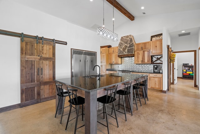 kitchen with tasteful backsplash, beamed ceiling, a center island with sink, a barn door, and built in fridge