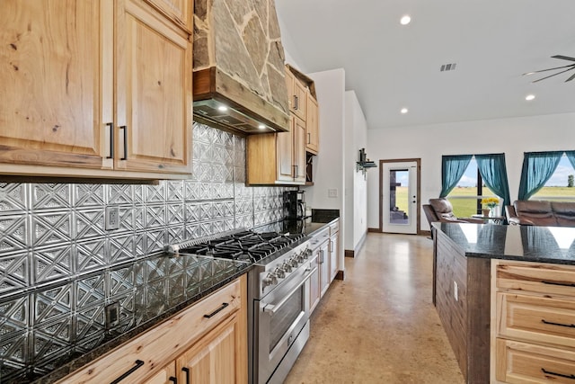 kitchen featuring premium range hood, high end range, decorative backsplash, dark stone counters, and light brown cabinets