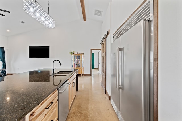 kitchen with dark stone countertops, stainless steel appliances, beam ceiling, pendant lighting, and sink