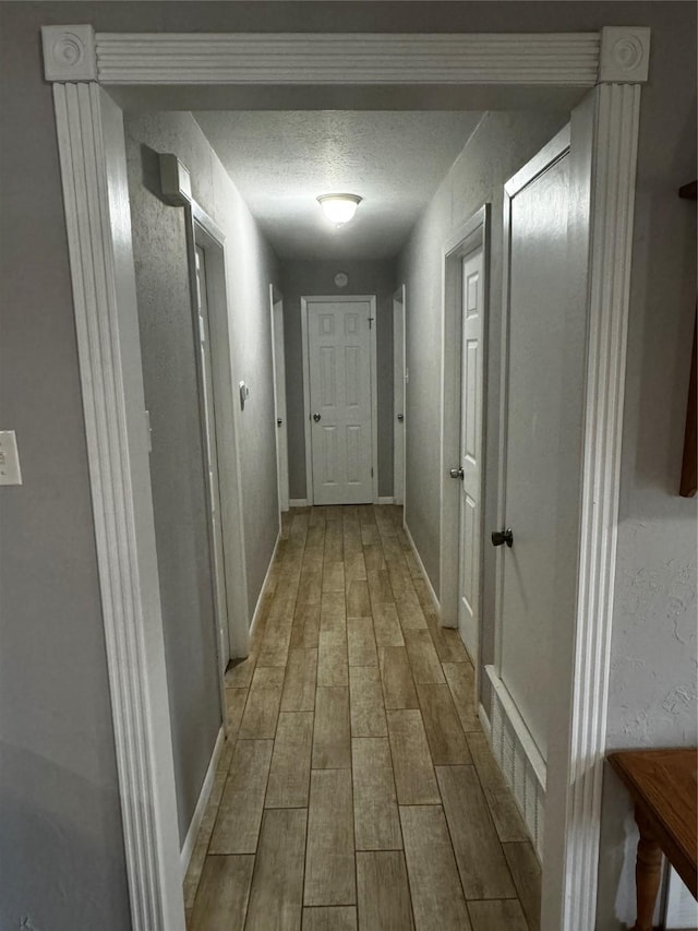 hallway with a textured ceiling and light hardwood / wood-style flooring