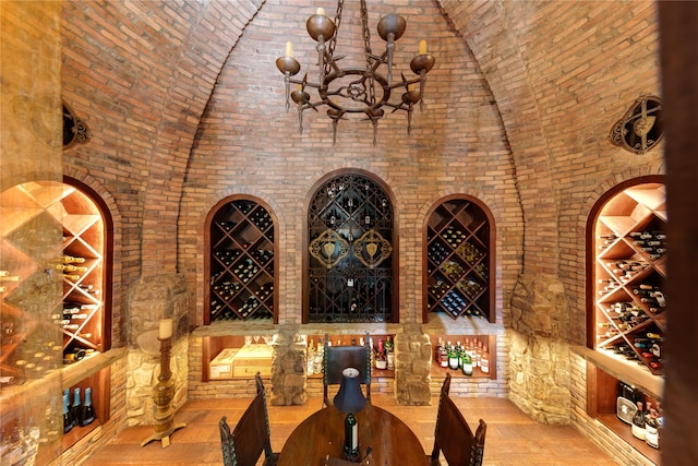 wine room featuring high vaulted ceiling, a chandelier, brick wall, and brick ceiling