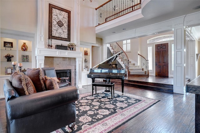 living room featuring built in features, a fireplace, a towering ceiling, and dark hardwood / wood-style flooring