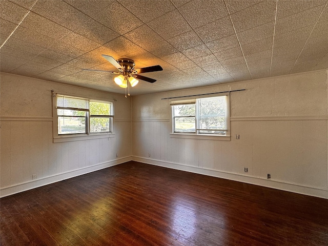 unfurnished room with a wainscoted wall, dark wood-style flooring, a ceiling fan, and a healthy amount of sunlight