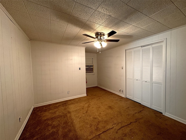 unfurnished bedroom featuring dark colored carpet, ceiling fan, wooden walls, and a wall mounted AC