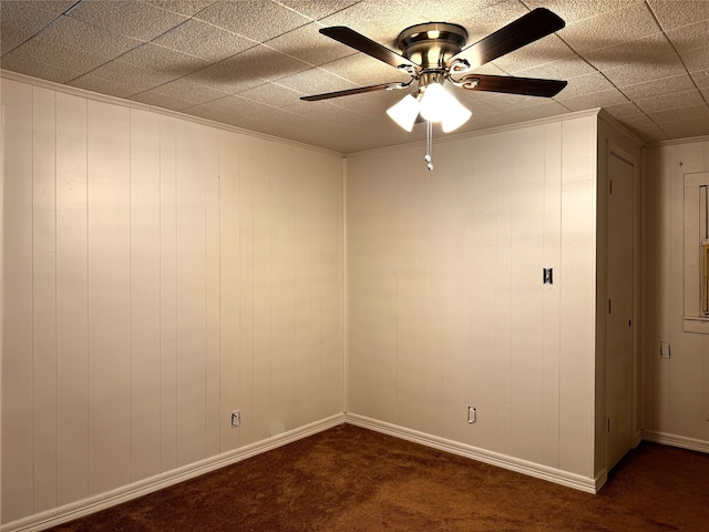 unfurnished room with wood walls, ceiling fan, and dark colored carpet