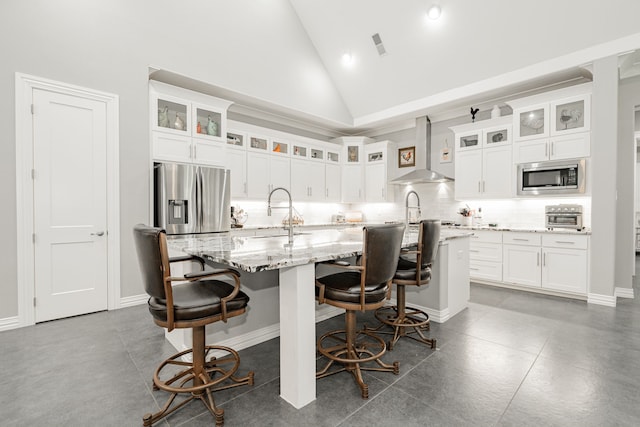 kitchen with stainless steel appliances, backsplash, high vaulted ceiling, wall chimney exhaust hood, and a kitchen island with sink