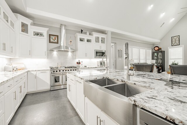 kitchen featuring wall chimney range hood, appliances with stainless steel finishes, white cabinets, backsplash, and light tile flooring