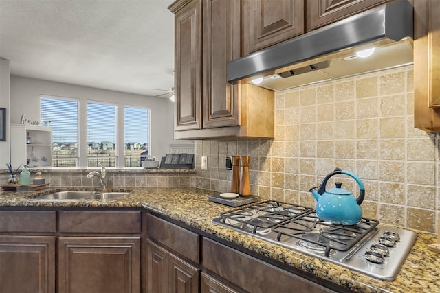 kitchen featuring tasteful backsplash, dark brown cabinets, under cabinet range hood, stainless steel gas cooktop, and a sink