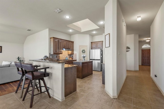 kitchen featuring visible vents, a skylight, freestanding refrigerator, and under cabinet range hood