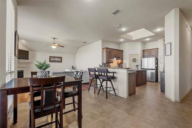 dining space with ceiling fan, recessed lighting, a fireplace, visible vents, and lofted ceiling with skylight