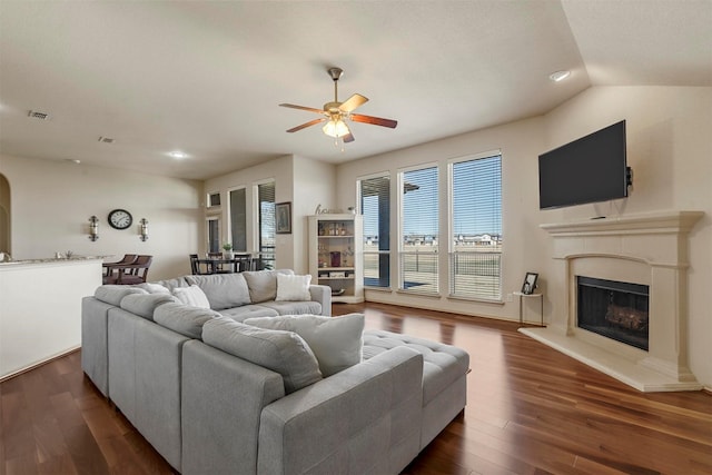 living room with visible vents, a fireplace with raised hearth, dark wood finished floors, a ceiling fan, and vaulted ceiling