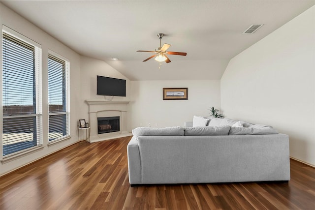 living room featuring a fireplace with raised hearth, visible vents, vaulted ceiling, and dark wood-type flooring