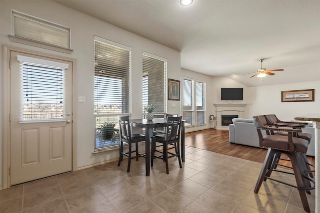 dining room featuring vaulted ceiling, ceiling fan, tile patterned flooring, and a glass covered fireplace