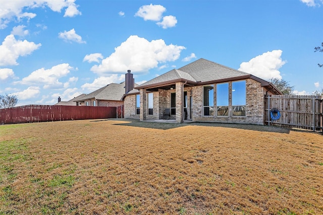 back of house with brick siding, a fenced backyard, a chimney, and a yard