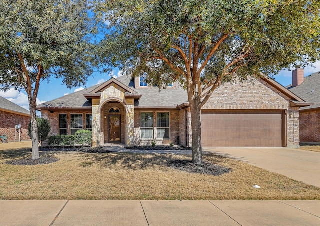 traditional-style house with a garage, brick siding, driveway, stone siding, and a front yard