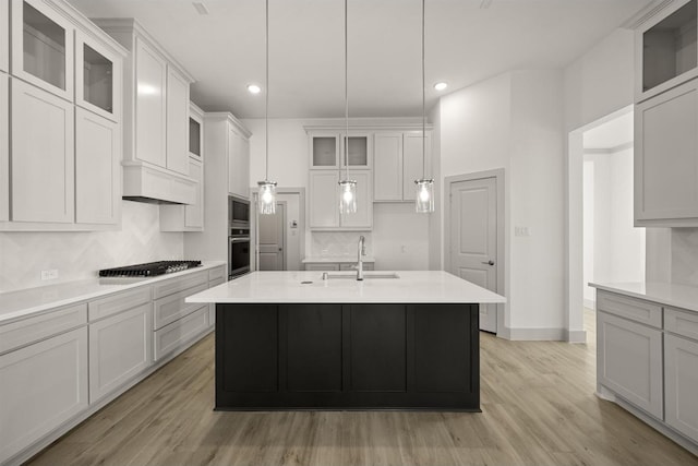 kitchen featuring light wood finished floors, light countertops, decorative backsplash, appliances with stainless steel finishes, and a sink