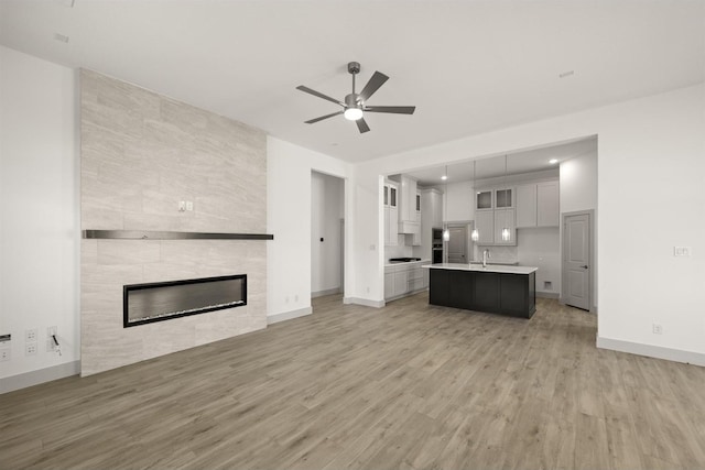 unfurnished living room featuring light wood-type flooring, baseboards, a tile fireplace, and ceiling fan