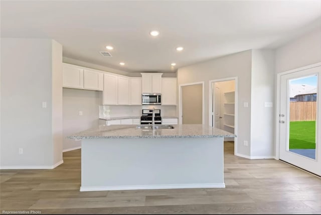 kitchen with a kitchen island with sink, light stone counters, and white cabinetry