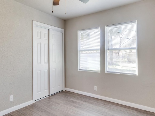 unfurnished bedroom featuring ceiling fan, light hardwood / wood-style flooring, multiple windows, and a closet