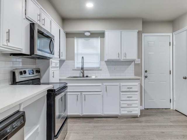 kitchen with sink, decorative backsplash, appliances with stainless steel finishes, light hardwood / wood-style floors, and white cabinetry