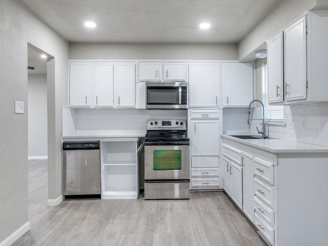 kitchen with sink, light wood-type flooring, appliances with stainless steel finishes, tasteful backsplash, and white cabinetry