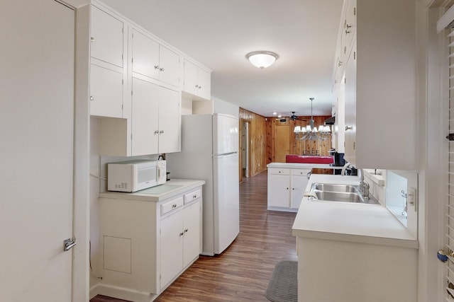 kitchen with white cabinets, kitchen peninsula, sink, white appliances, and dark hardwood / wood-style flooring