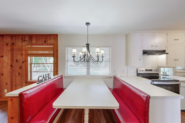 kitchen with white cabinetry, dark wood-type flooring, stainless steel electric range, wood walls, and pendant lighting