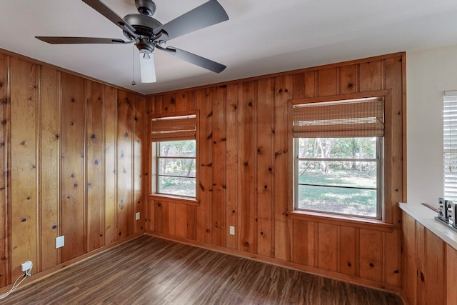 empty room featuring ceiling fan, wooden walls, dark hardwood / wood-style flooring, and a healthy amount of sunlight