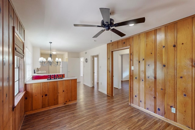 kitchen featuring pendant lighting, wooden walls, ceiling fan with notable chandelier, and dark wood-type flooring