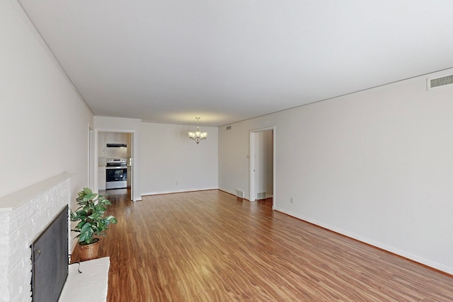 unfurnished living room with a brick fireplace, hardwood / wood-style flooring, and a notable chandelier