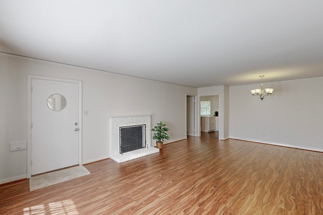 unfurnished living room featuring a brick fireplace, hardwood / wood-style flooring, and a notable chandelier