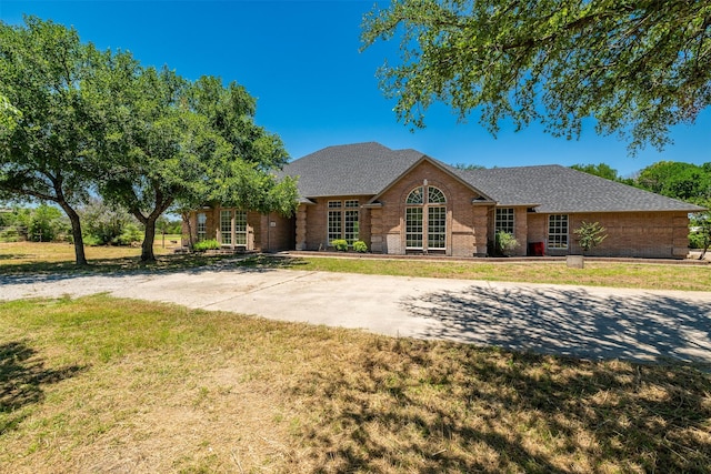 view of front of house featuring brick siding, a shingled roof, and a front yard