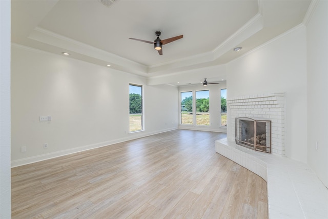 unfurnished living room featuring ceiling fan, a raised ceiling, crown molding, a fireplace, and light wood-type flooring