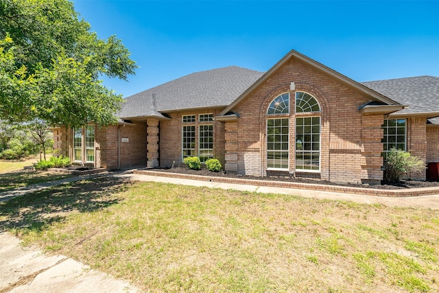 ranch-style house with a shingled roof, brick siding, and a front lawn