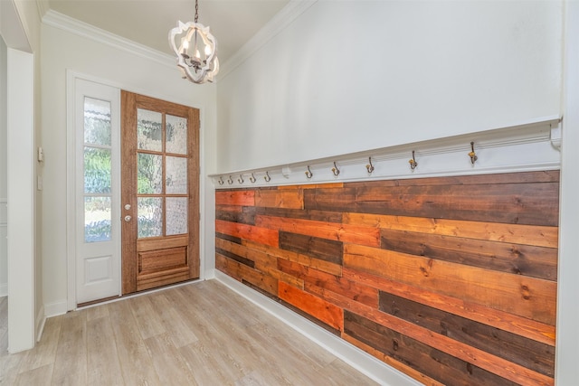 doorway with ornamental molding, baseboards, a notable chandelier, and light wood finished floors