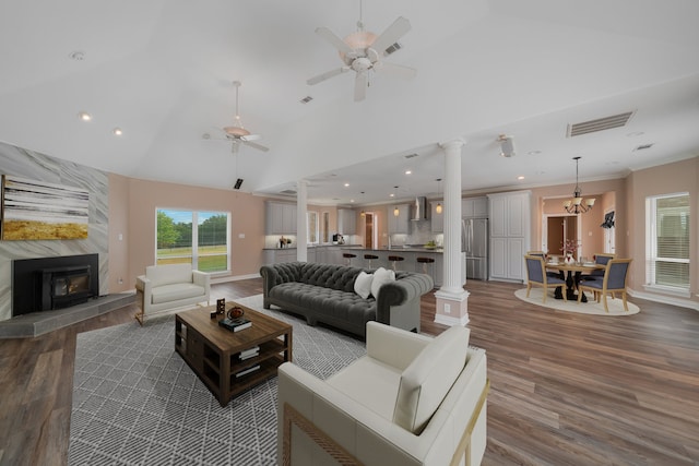 living room with high vaulted ceiling, ceiling fan with notable chandelier, dark hardwood / wood-style floors, ornate columns, and a tiled fireplace