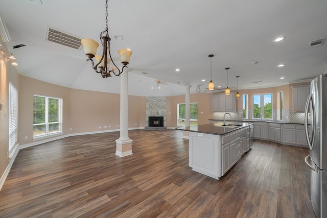 kitchen with stainless steel refrigerator, gray cabinetry, dark wood-type flooring, a high end fireplace, and an island with sink