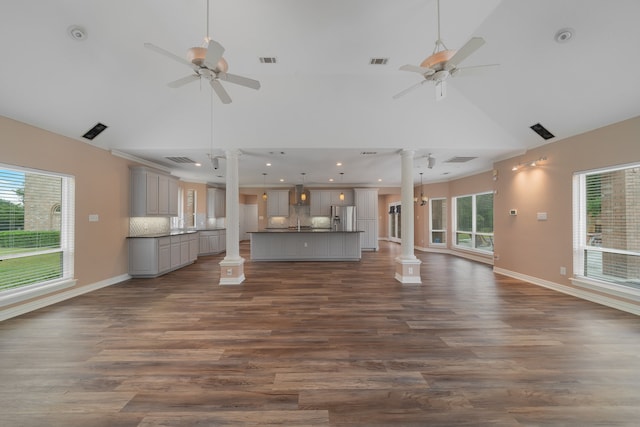 unfurnished living room featuring dark hardwood / wood-style floors, ceiling fan with notable chandelier, high vaulted ceiling, and decorative columns