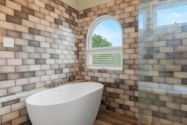 bathroom with a wealth of natural light, a washtub, and tile walls